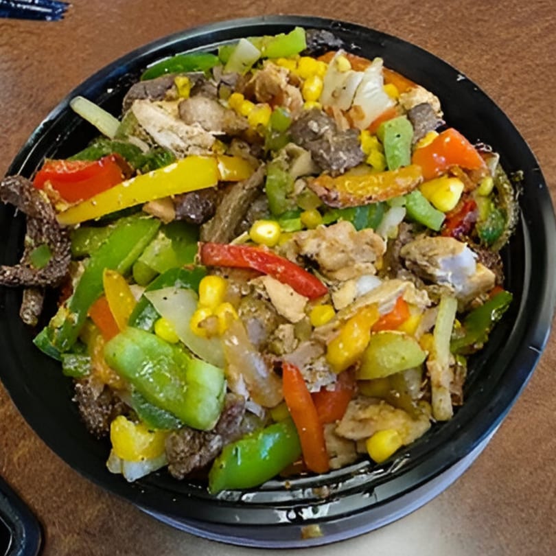 A black bowl filled with colorful American cuisine, including bell peppers, corn, onions, and meat.