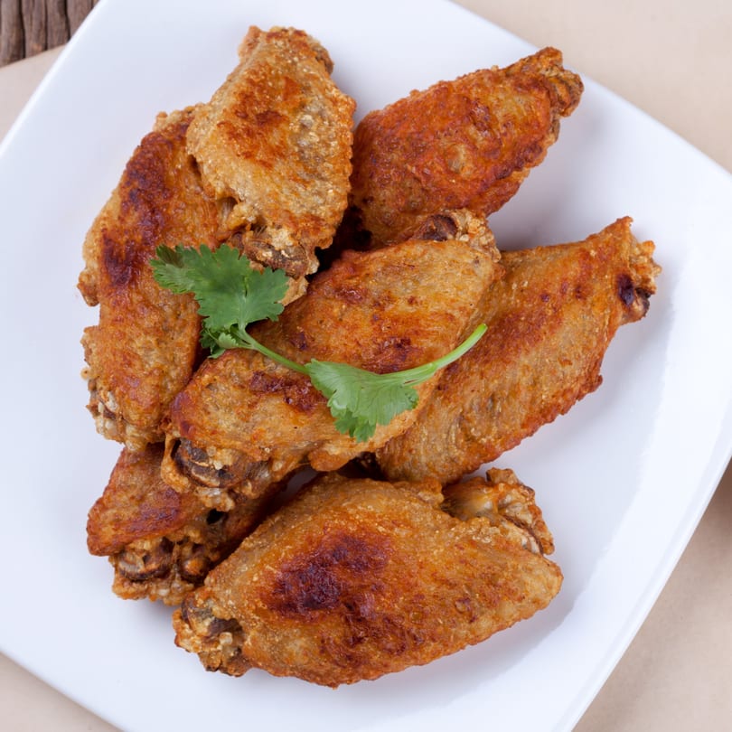 Crispy fried chicken wings, garnished with fresh cilantro, on a white rectangular plate.