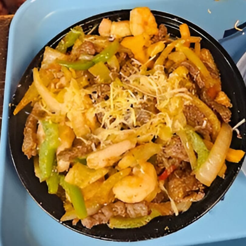 A black bowl of Twisted Potatoes with meat, green peppers, onions, and shredded cheese on a blue tray.