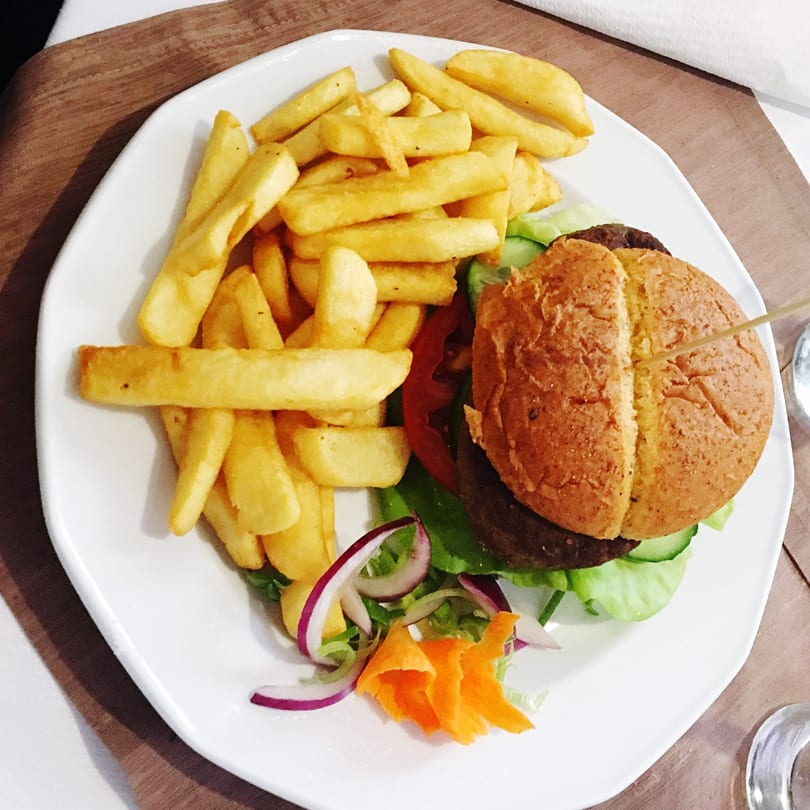 A burger with fries, lettuce, tomato, cucumber, red onion, and carrot on a white plate.