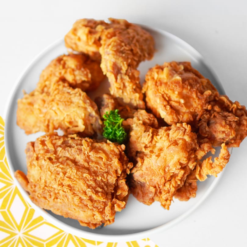 Crispy fried chicken pieces with a sprig of parsley on a white plate, with a yellow patterned napkin.