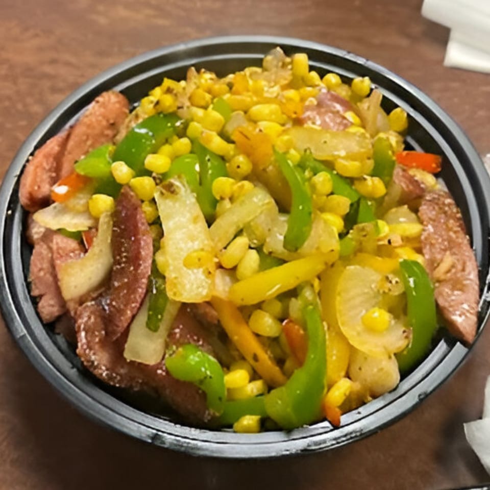 A black bowl filled with sliced sausage, corn, and sautéed green and yellow bell peppers.